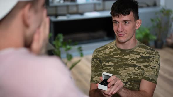 Portrait of Smiling Young Gay Man on One Knee Making Proposal to Boyfriend Opening Ring Box As