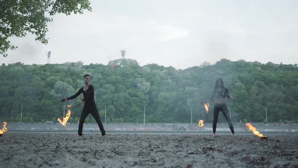 Young Beautiful Girl and Handsome Man in Black Clothes Performing Show with Flame Standing