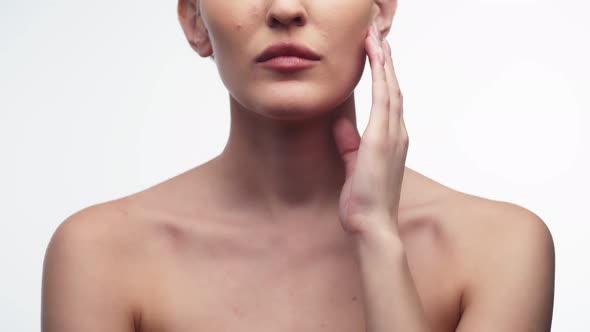 Woman Runs Finger Along Chin After Using Cosmetic Cream While Standing on White Background in Studio