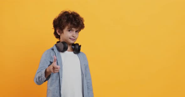 Cool Curly Boy with Headphones on Neck Indicating Happily at Camera, Flirt Concept