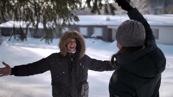A Young Woman Shakes a Pine Branch with Snow on Her Man, Male Hugs Female