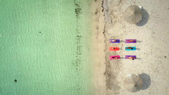 Aerial view of group of people in yoga pose on colourful mats on the beach.