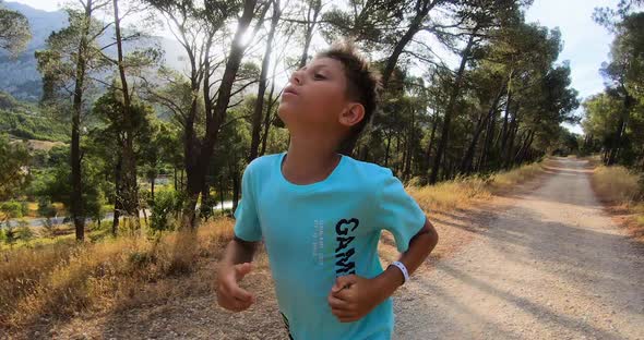 Young Boy Running in Path of Park on Background of Trees and Rocky mountains.