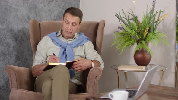 Middle-Aged Relaxed Caucasian Man Writing in Journal at Home