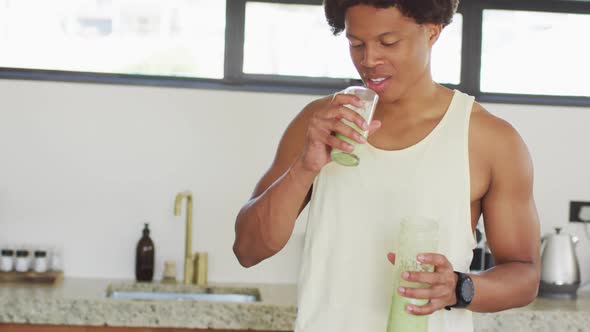 Fit african american man cooking, drinking healthy green smoothie