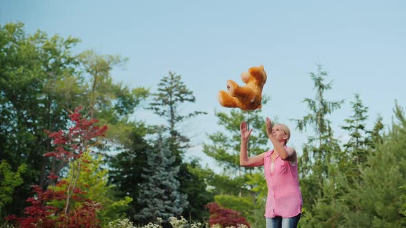 Middle Aged Woman Having Fun Like a Child - Jumping on a Trampoline and Throwing Up a Teddy Bear