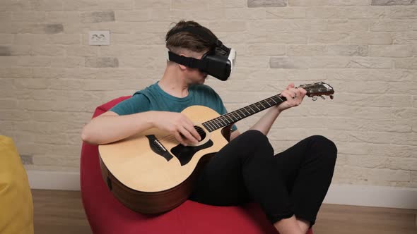 Young Man Sitting on Bean Bag with the Vr Glasses Is Playing at the Guitar.