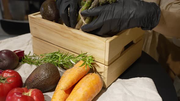 Woman in Rubber Gloves Fills Wooden Box with Vegetables