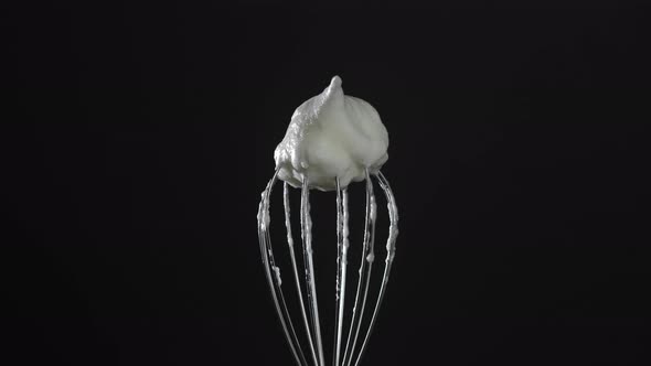 Metal whisk with whipped egg whites, isolated on black background