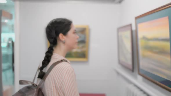 Portrait of young caucasian thoughtful woman looks at the painting. Exhibition in the art gallery.