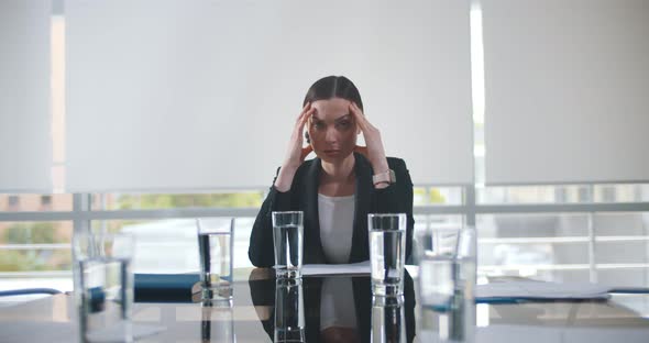 Tired Office Employee in Suit Having Headache Sitting in Empty Conference Room