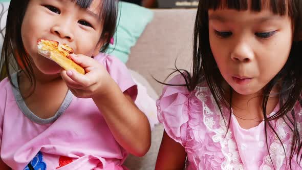 Cute sibling girls eating pizza. Hungry kids taking a bite from pizza on a pizza party at home.