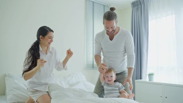 Caucasian loving parents, young couple play with baby boy child and dance together on bed in bedroom