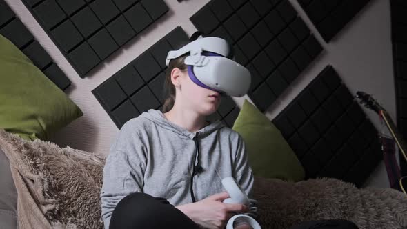 Young Woman Sitting on Sofa Playing Game Using VR Helmet Indoor at Home