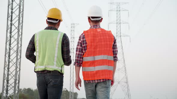 Asian engineer and foreman discussed a high voltage electricity pylon at sunset background.