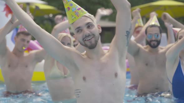 Close-up of Cheerful Young Tattooed Man with Blond Dyed Hair Dancing and Spinning in Water at Resort