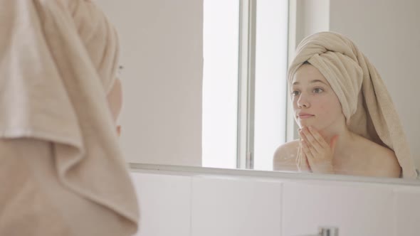 Teenage girl looking at the mirror in the bathroom - checking her face