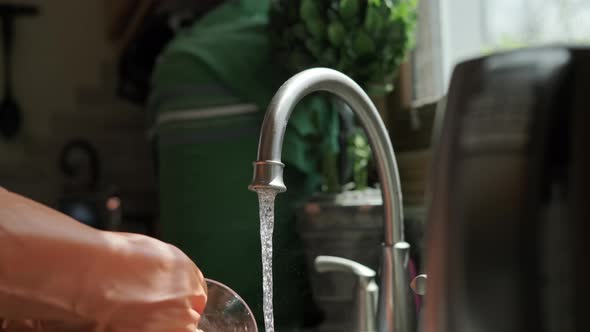 Hands in Orange Gloves Wash Dishes in the Kitchen