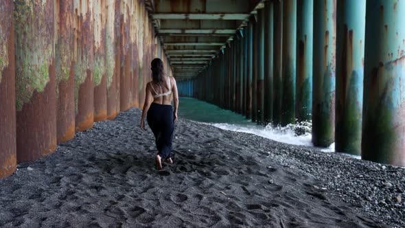 a Barefoot Woman Dances Under the Pillars of the Bridge Against the Background of the Incoming Waves