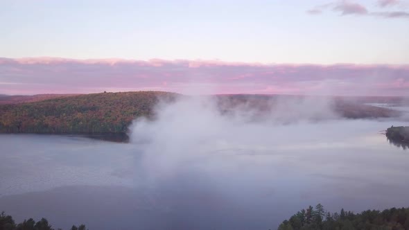 Aerial Sunrise Wide Shot Flying Through Cloud Fog Showing Misty Lake And Pink Clouds And Fall Forest