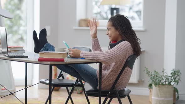 Wide Shot of Relaxed Teenage African American Girl with Feet on Table Surfing Social Media on