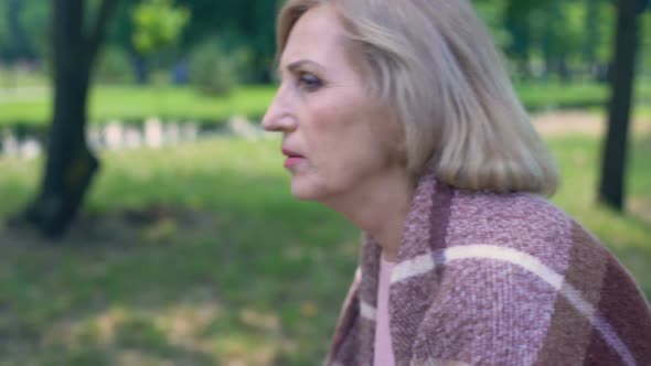 Thoughtful Aged Lady Covered With Plaid Blanket Sitting on Bench in Garden