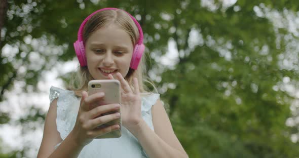 Happy Teenager Making Online Video Call with Modern Pink Headphones in Park