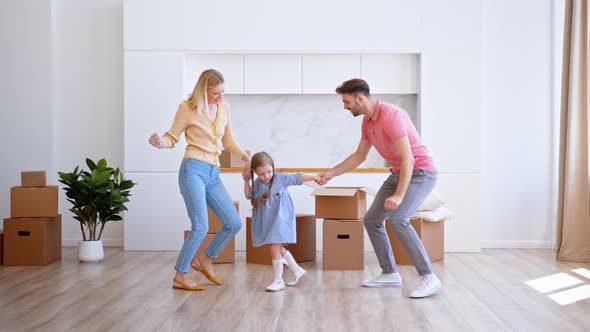 Amazed family parents and preschooler daughter dance on new apartment floor