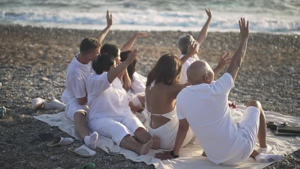 Back View of Happy Asian Multigenerational Family Waving to Sunset Sitting on Rocky Mediterranean