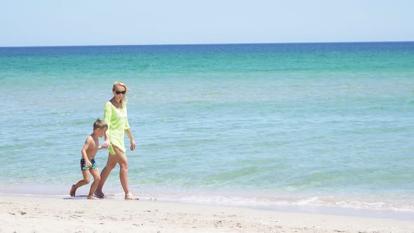 Little Boy Holding His Mother's Hand Walks Along the Sandy Shore of the Azure Sea