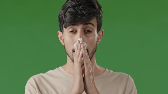 Closeup in Studio with Green Background Sick Hispanic Guy Sneezes Wipes with Paper Napkin Young Man