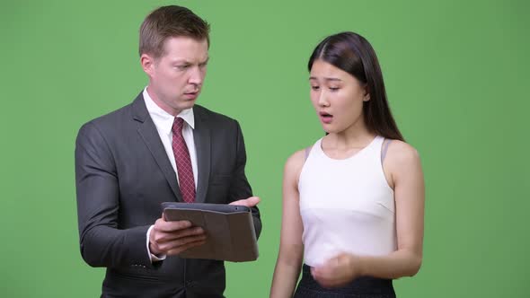 Young Businessman Showing Bad News To Young Asian Businesswoman