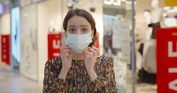 Portrait of Young Woman Putting on Safety Mask Standing in Shopping Mall Hall