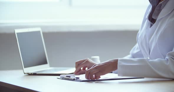 Side View of Woman Doctor Sitting at Table Near Laptop, Female Hands Writes Appointment To Patient