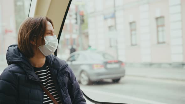 A Young Woman Wearing a Facial Mask Looking at the Window While Riding a Bus