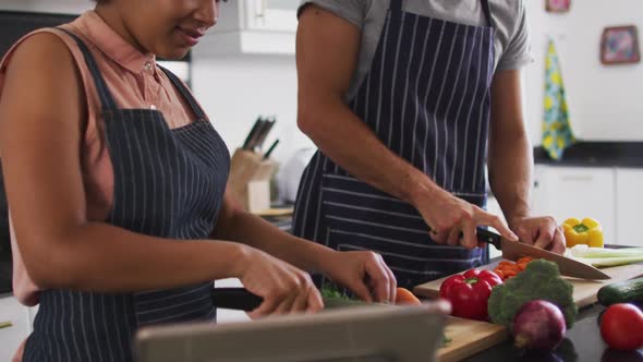 Mixed race couple wearing aprons chopping vegetables together in the kitchen at home