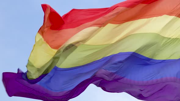 The rainbow flag, LGBT pride flag gay pride flag waving in the wind blue sky close up 4k