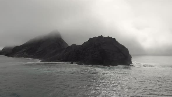 Big rock shrouded in mist in open sea near Ponta da Calheta beach, Portugal. Aerial circling