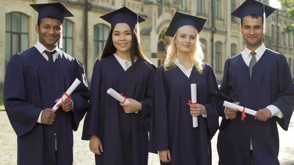 University Graduates in Academic Regalia Holding Diplomas, Putting Thumbs-Up
