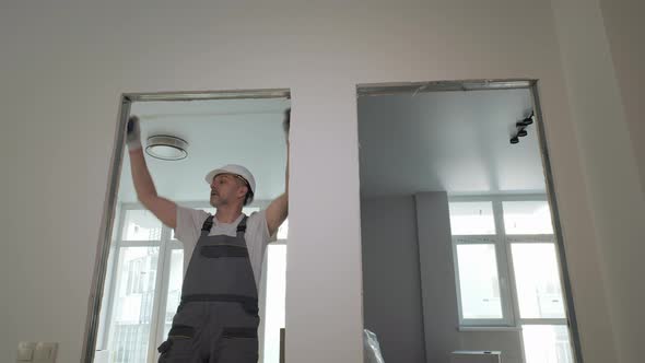 A Builder in Working Uniform Checks the Size and Quality of Doorways in a New Apartment