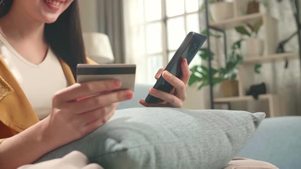 Woman Sitting On Couch In Living Room Holding Credit Card And Using Smartphone Shopping Online