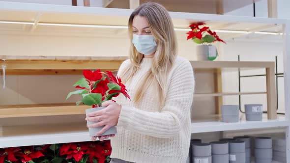 a Young Woman in a Protective Mask in a Store Twists a Astralis or Poinsettia Christmas Flower in