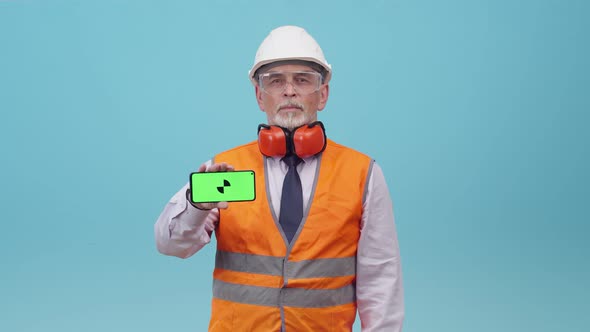 Adult Man Engineer with Protective Helmet and Working Uniform Shows Phone Screen with an App the