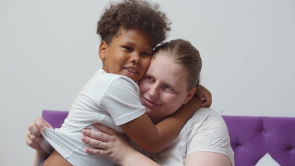 Portrait of Caucasian Mother and Mixed Race Little Son Hugging Sitting on Bed