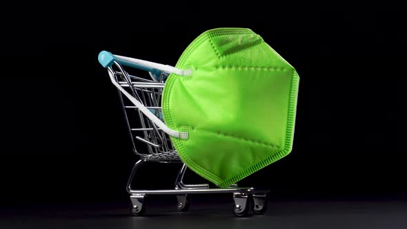 Shopping cart with a colorful green medical mask kn95 dressed on a metallic shiny basket.