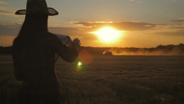 Farmer Woman with Tablet Working in Wheat Field During Harvesting By a Combine, She Controls the