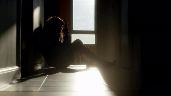 Silhouette of Frustrated Woman with Long Hair Sitting in Corridor at Sunrise or Sunset