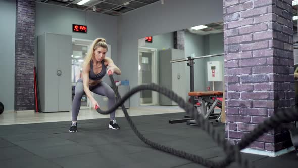 Young sporty woman working out with Fitness battling ropes at gym