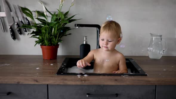 Cute Happy Baby Girl with Playing with Water and Foam in a Kitchen Sink at Home