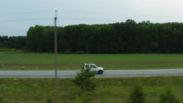 Aerial View of a Car Driving Along the Road Among Fields of Green Grass